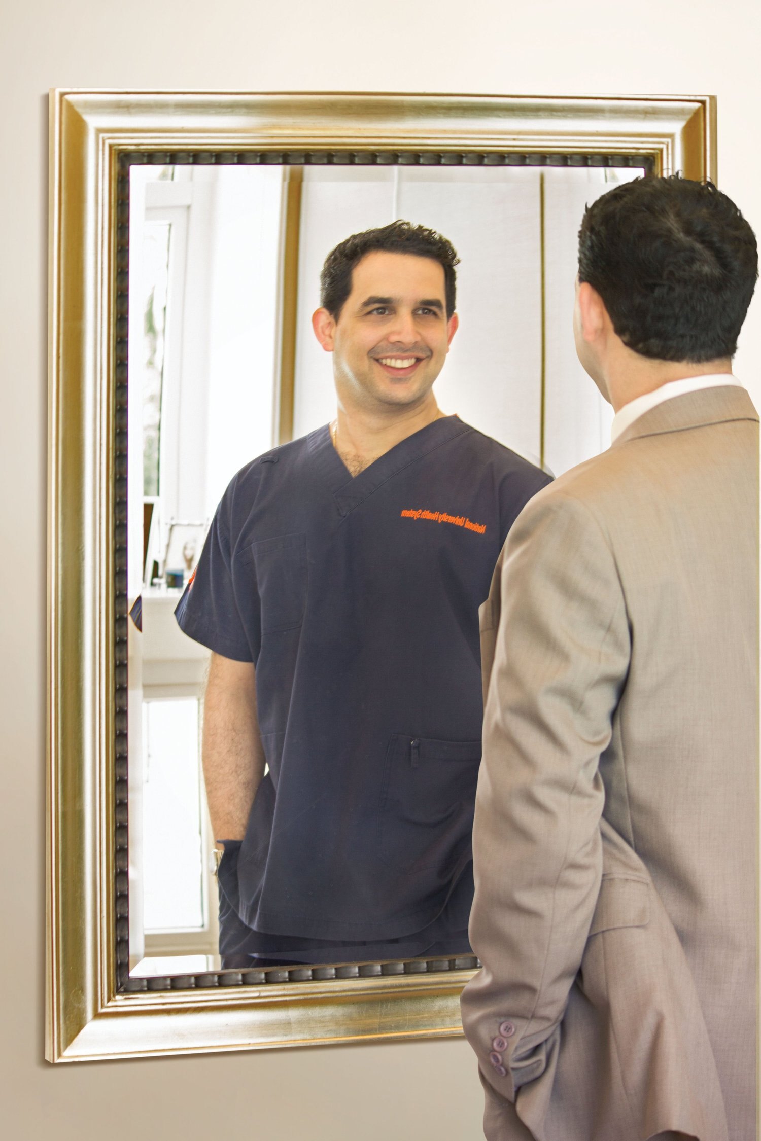 Dr. Zubin J Daruwalla in a suit, his reflection showing him in hospital scrubs